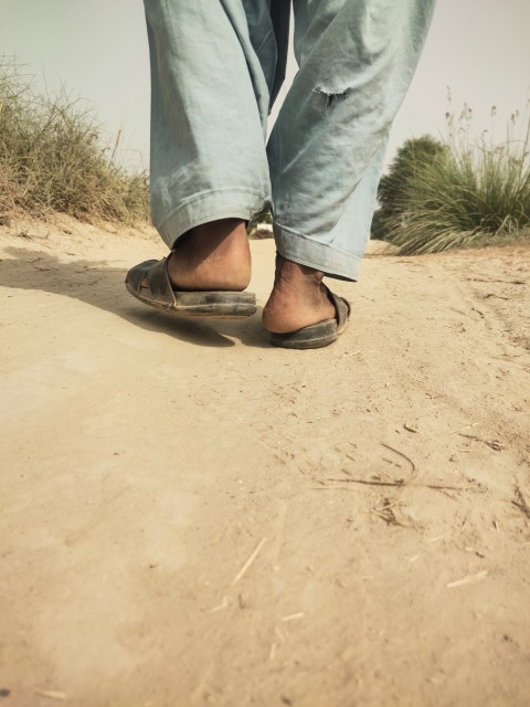 A boy walks on the dirt road of the village with one foot on the ground and the other in the air