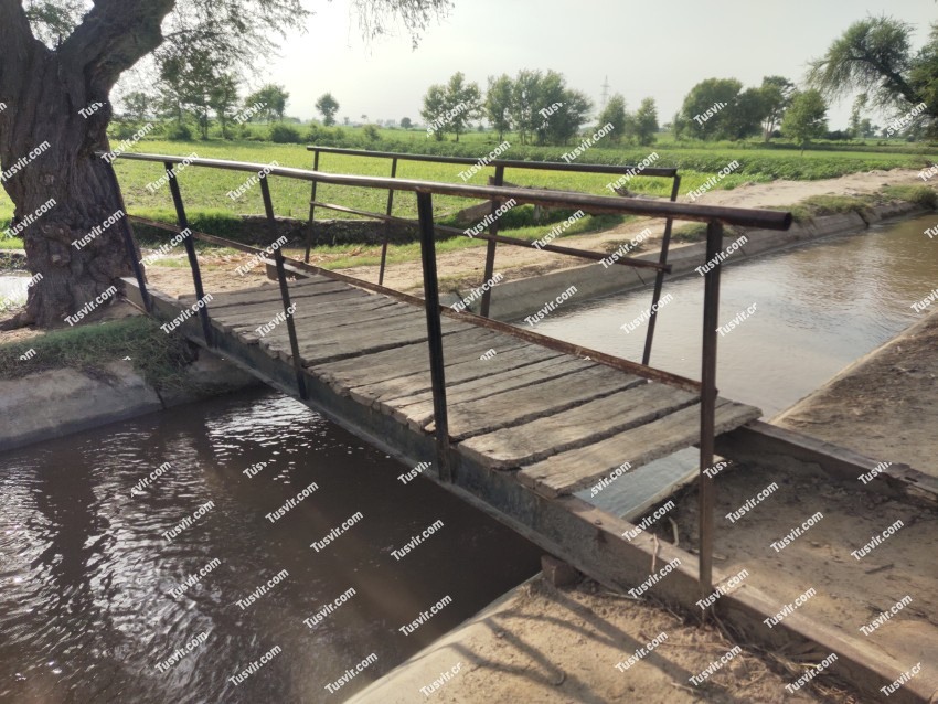 A bridge made of iron and wood over a flowing canal, A bridge side view