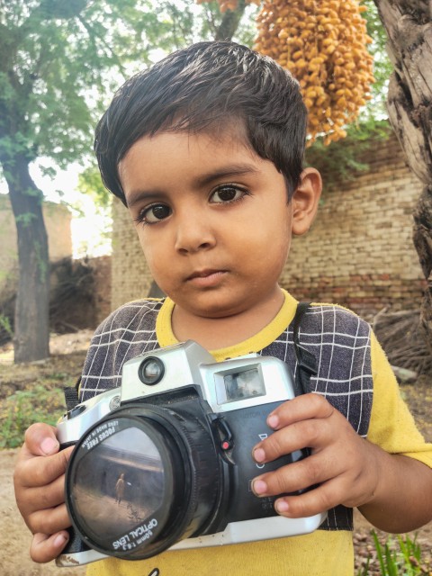 A child holding a camera in his hand is taking a picture with a mobile phone.