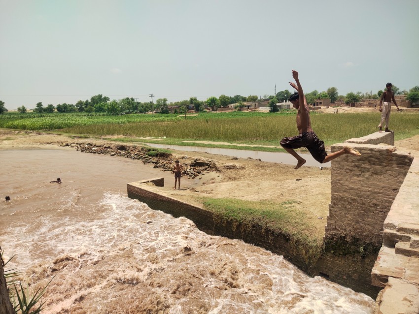 A child is jumping from a height to dive into the flowing water of a canal.