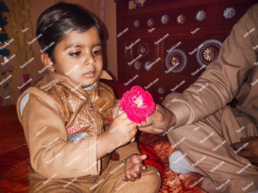 A child sitting on a bed giving red flowers to an elderly man
