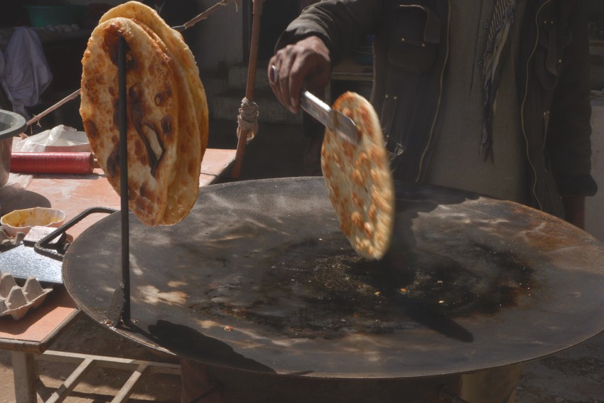 A hand holding a paratha in chimta or tong.