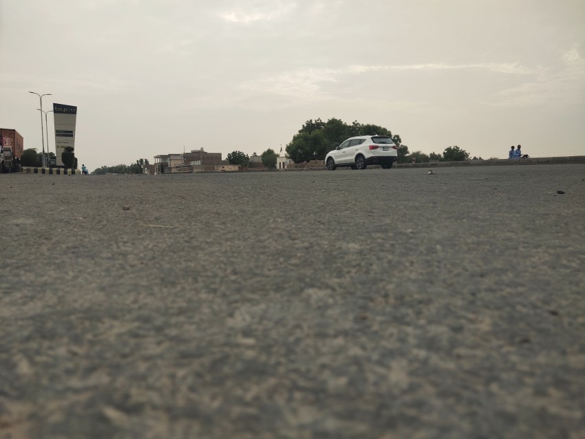 A picture of a white car driving on the National Highway which was going on an empty road