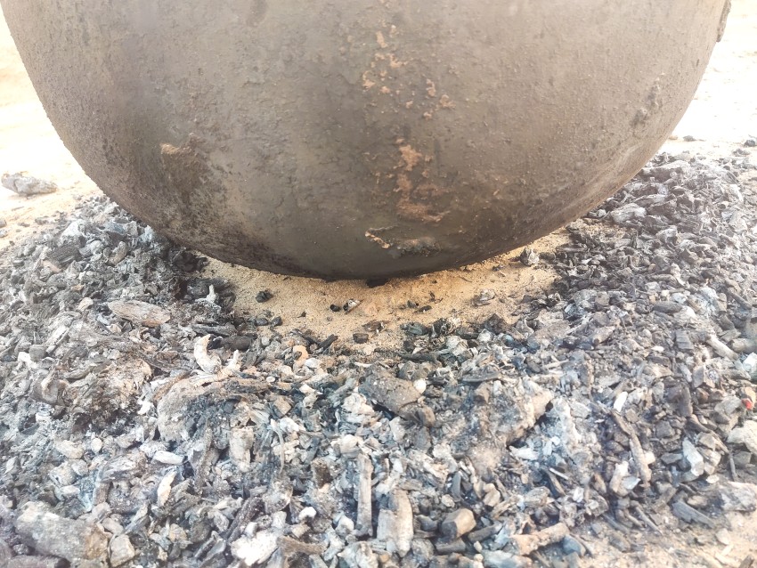 A pot of yolk placed on a tail and coals placed in a circle outside it