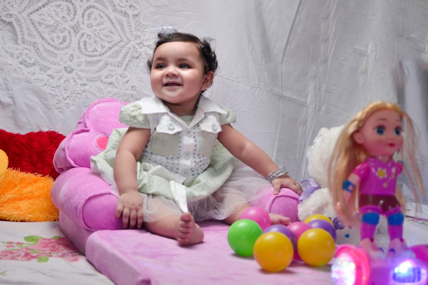 Baby photography   sitting like a queen while resting her arms with several colored balls and a doll in surrounding