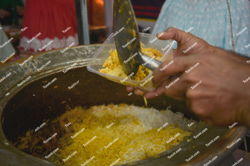 Catering serving biryani from a daig in a plastic box with bare hands using serving spoon