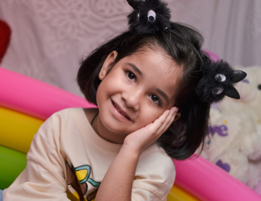 Preschooler leaning on her left hand acting as trying to sleep while smiling