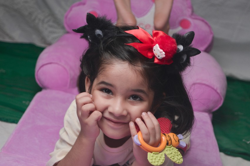 Preschooler looking up with raised legs with left hand holding a toy with red hair band