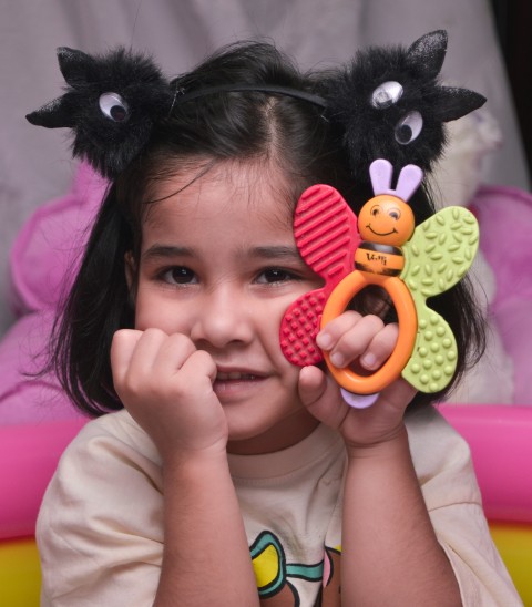 Preschooler with her right hand on her right cheek and holding a toy in her left hand