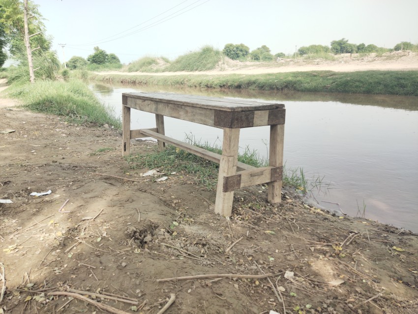 Side view of a wooden table is placed by the canal in the shade of a tree.