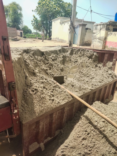 The gray sand has to be removed from the rickshaw with the help of a shovel.