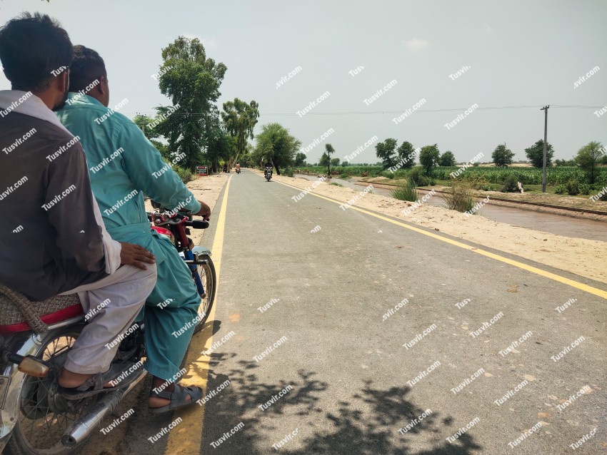 Two men on a motorcycle are looking at a flowing canal and a road